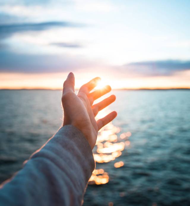 A vertical shot of a hand with the beautiful sea in the background during suns